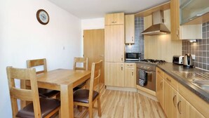 Een kleine keuken met houten kastjes, een magnetron, een fornuis en een spoelbak.