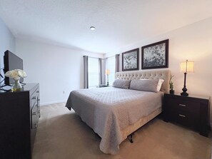 Une chambre à coucher avec un grand lit, une commode, une table de chevet avec une lampe, et deux tableaux encadrés au mur.