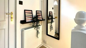 A hallway with a white door, a radiator, a black-framed mirror, and two framed pictures on a shelf. - Charming Home Near Gatwick Airport (Crawley)