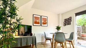 A modern living room with a flat-screen TV, a dining table with chairs, and a potted plant. - Charming Home Near Gatwick Airport (Crawley)