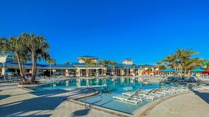 Ein Poolbereich eines Resorts mit Liegestühlen, Palmen und blauem Himmel.