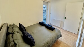 Un dormitorio con cama, almohadas, un radiador, una puerta y una ventana.