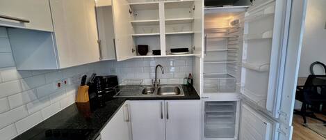 Een kleine keuken met witte kastjes, een zwart aanrecht, een ingebouwde vaatwasser en een koelkast met verschillende compartimenten.