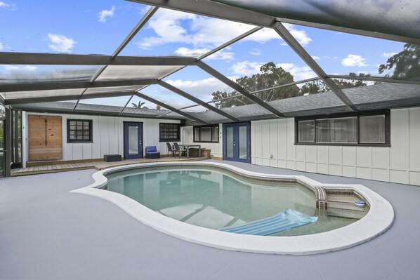 A covered swimming pool with a wooden door, a window, and a chair outside.