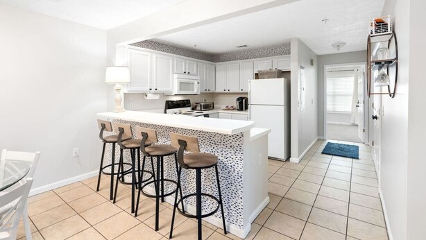 A modern kitchen with a central island, bar stools, white cabinetry, and a tiled floor. - *Family Stay 2 minutes to downtown Sleeps 10 (Auburn)