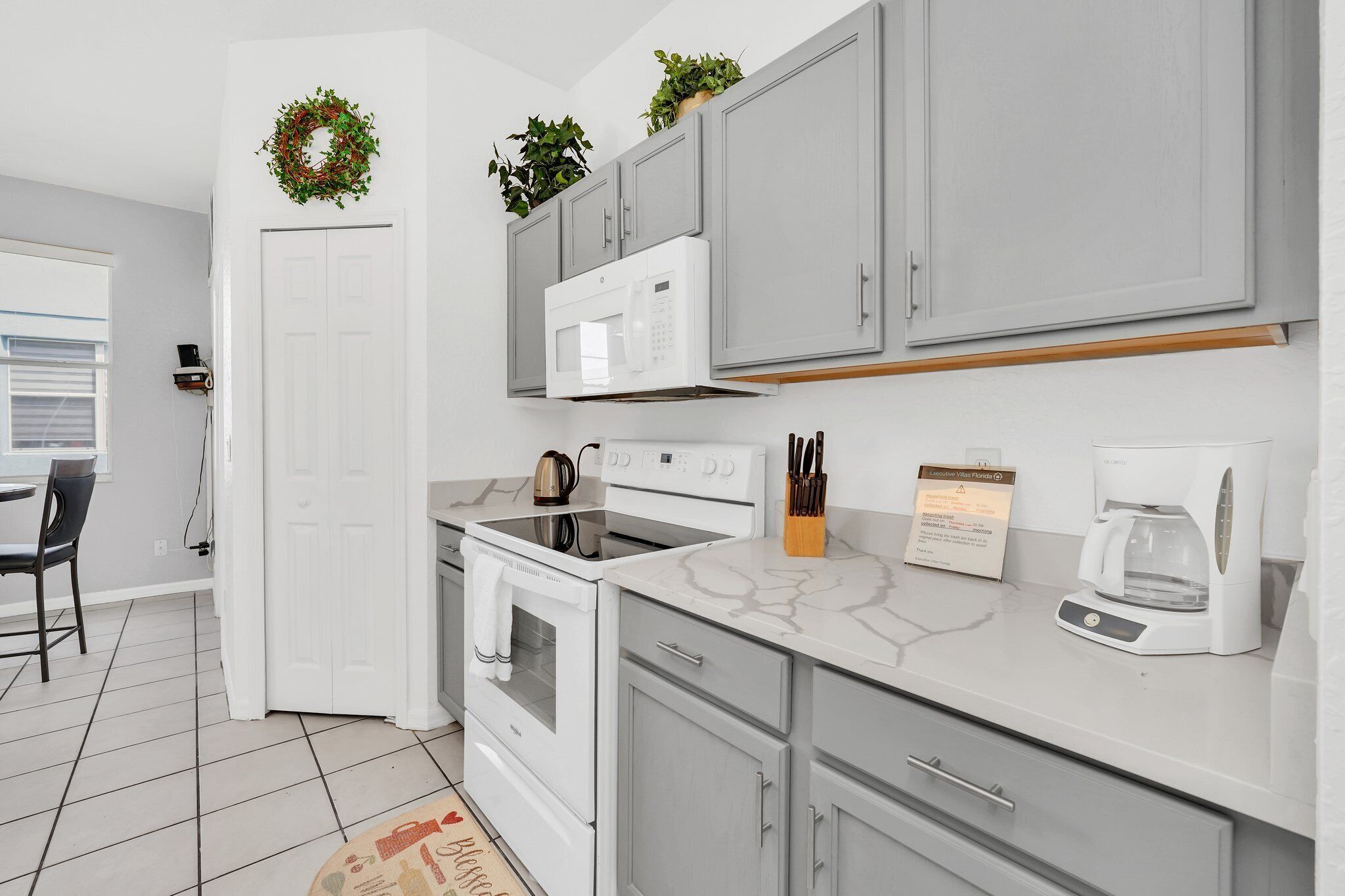 A modern kitchen with grey cabinets, white appliances, and a marble countertop.