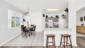 A modern kitchen with white cabinets, a central island, and a dining area with a table and chairs. - New Listing! Highlands Reserve Resort, 7mi to Disney & 17mi to Universal - FS379833 (Davenport)