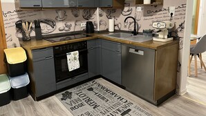 Cocina compacta con armarios grises, encimera de madera, lavavajillas integrado, cafetera y salpicadero con ilustraciones relacionadas con el café.