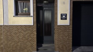 Entrada de un edificio con una puerta negra, una ventana pequeña con persianas verticales y un letrero de bienvenida.