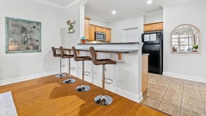 Une cuisine moderne dotée d’un îlot central, de meubles en bois, d’un réfrigérateur noir et de trois tabourets de bar.