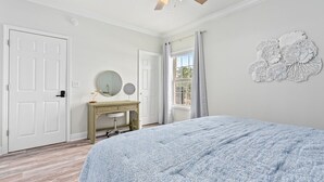 Une chambre à coucher comprenant un lit, un ventilateur de plafond, une commode, un miroir et une fenêtre avec des rideaux.