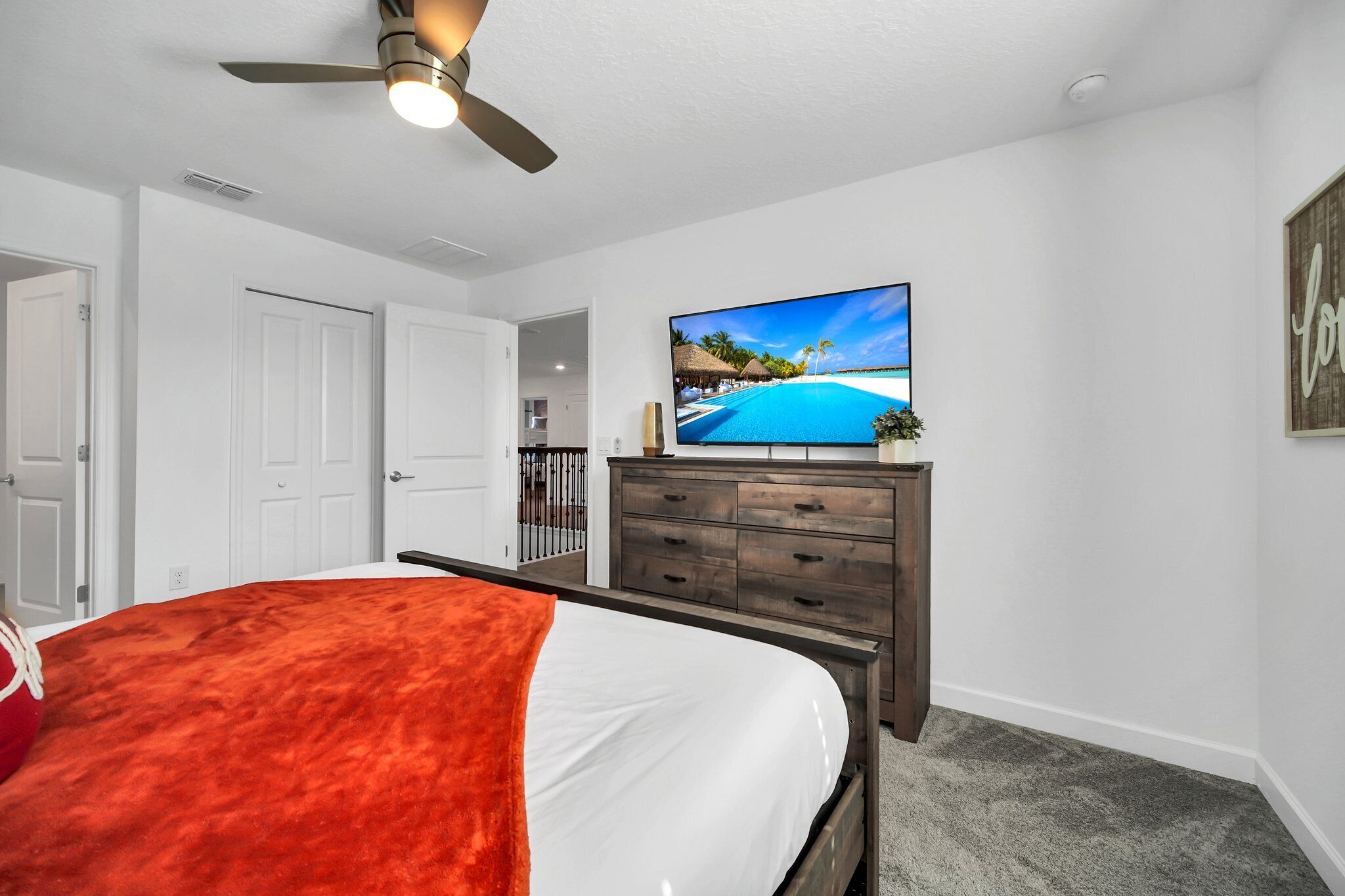 A bedroom with a bed, a television, a ceiling fan, and a view of a beach.