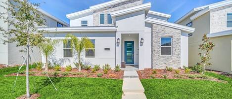 A modern two-story house with a stone facade, a green door, and a well-maintained lawn.