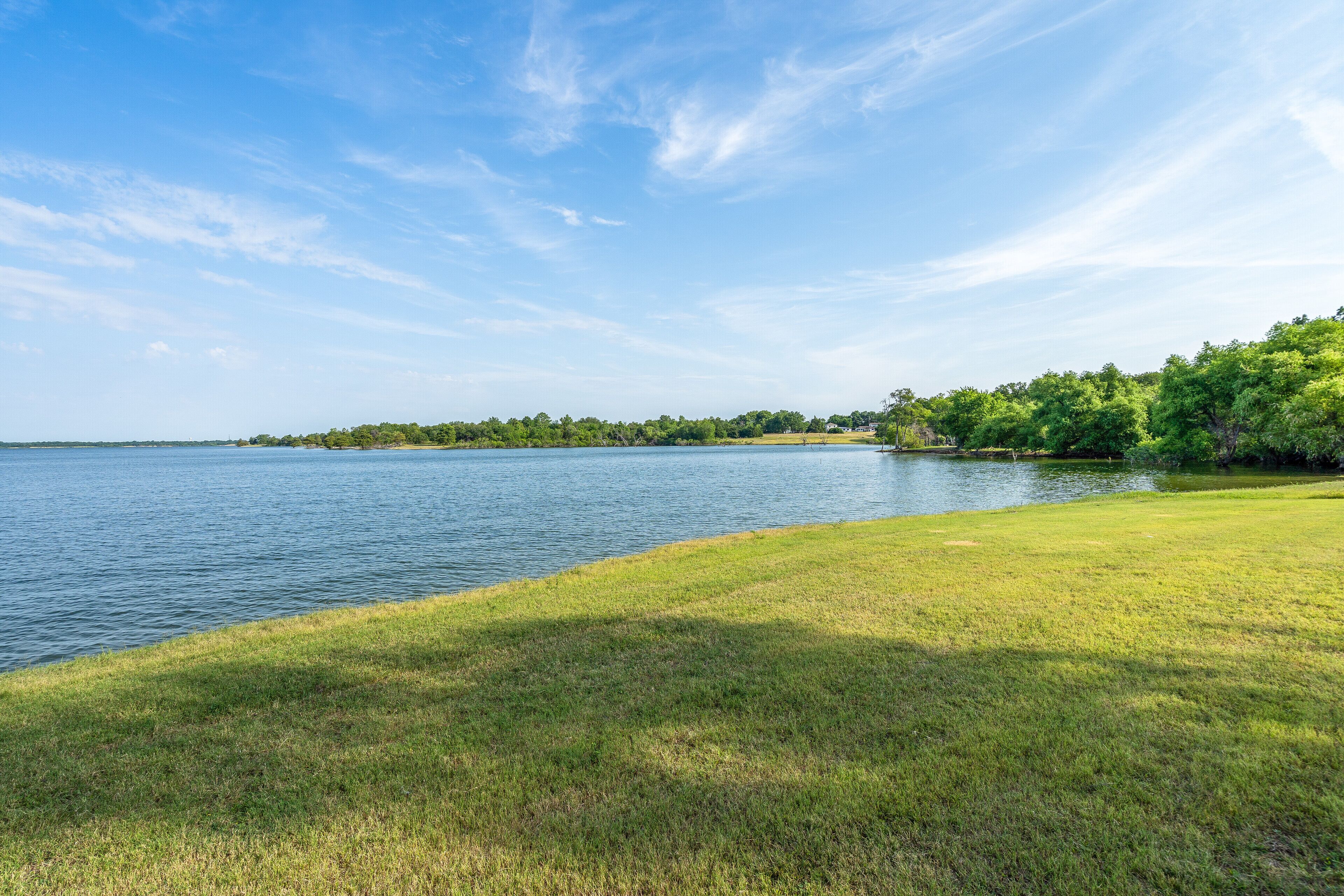 A lakeside view with grassy banks and trees in the background.