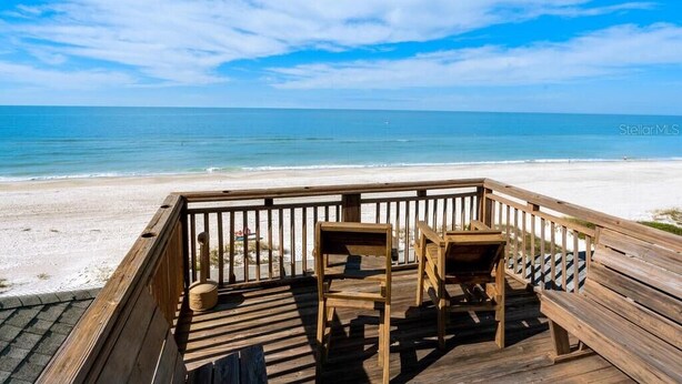 Een houten terras met twee stoelen met uitzicht op een strand.