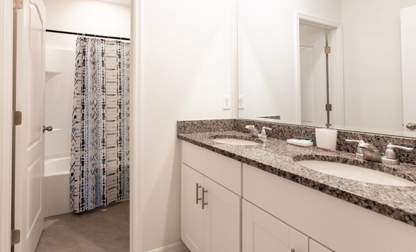 Bathroom features two sinks, a large mirror, and a shower with a patterned curtain.