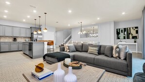 Een moderne woonkamer met een grijze bank, een salontafel en een keuken met grijze kastjes en een backsplash van baksteen.