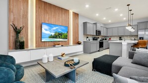Een moderne woonkamer met een televisie, bank, salontafel en een keuken op de achtergrond.