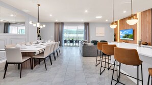 Een moderne eetruimte met een grote tafel voor zes personen, een bar met krukken, en een aan de muur bevestigde televisie.