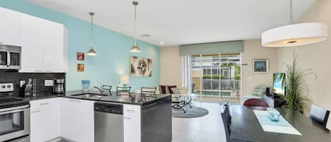 A modern kitchen with white cabinets, a central island, stainless steel appliances, pendant lighting, and a dining area with a large table and chairs.