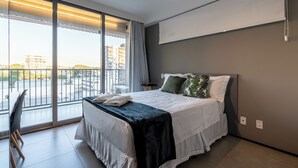 Ein modernes Hotelzimmer mit einem großen Bett, einem Balkon mit Blick auf Gebäude und einem Schreibtisch mit Stuhl.