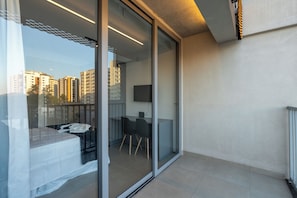 A modern balcony with a glass door, a small table, two chairs, and a TV mounted on the wall.