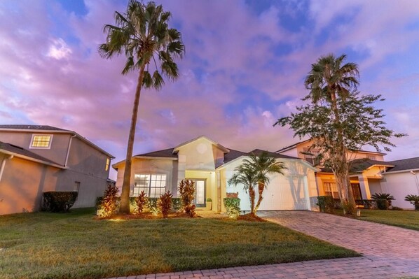 A residential house with a well-maintained lawn, palm trees, and a paved driveway.