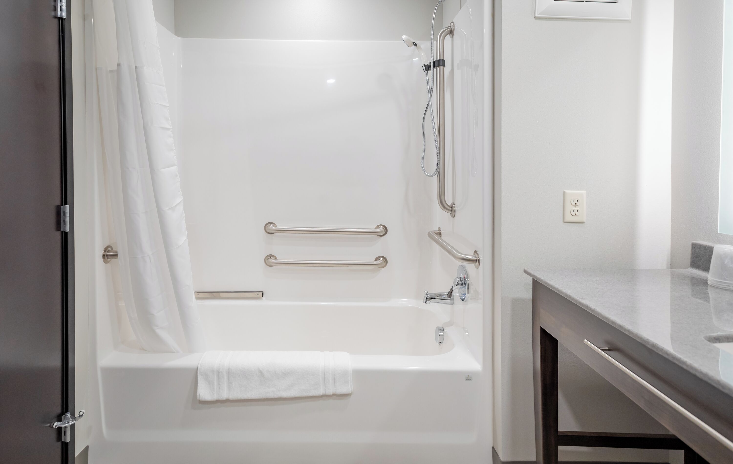 A modern bathroom with a white bathtub, grab bars, and a shower curtain.