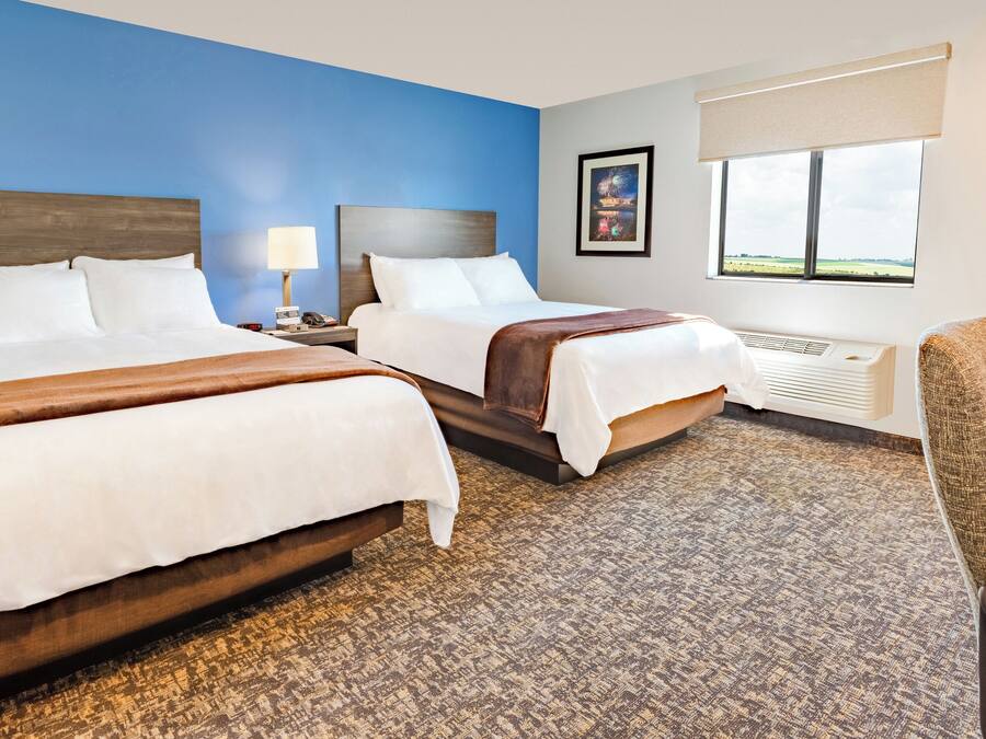 A hotel room with two beds, a large window with a view, a heater, and a chair.