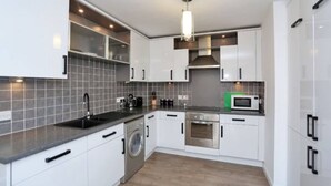A modern kitchen with white cabinets, a built-in washing machine, a microwave, and a stainless steel oven.