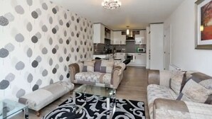 A living room with a patterned wall, a sofa, a glass coffee table, and a rug.