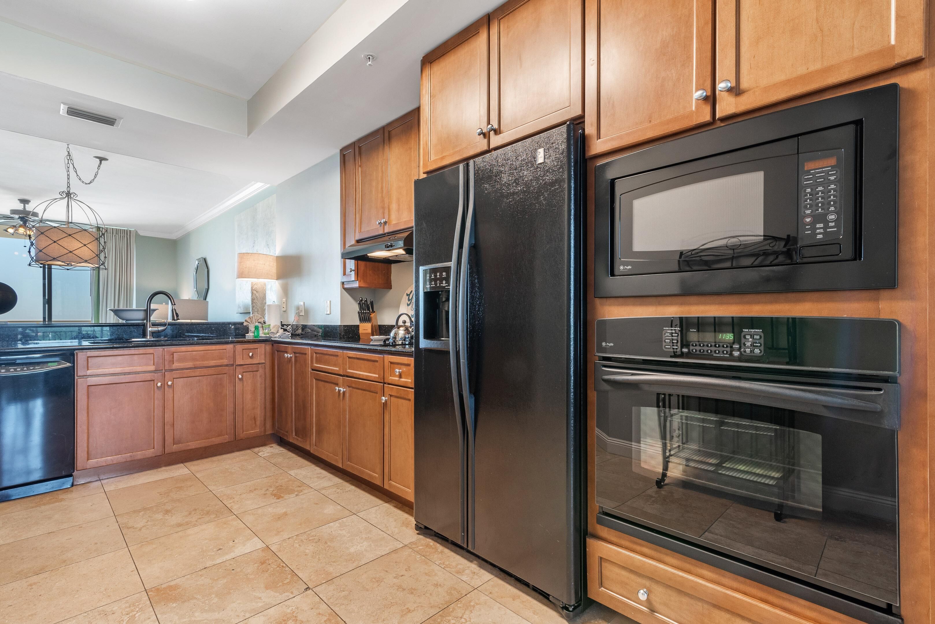 A modern kitchen with wooden cabinets, a stainless steel refrigerator, a built-in microwave, and an oven.