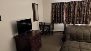 A hotel room with a bed, a TV on a dresser, a desk with a chair, and a window with curtains.