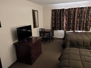 A hotel room with a bed, a TV on a dresser, a desk with a chair, and a window with curtains. - Minnedosa Inn (Minnedosa)