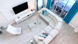 Un salon moderne avec un grand téléviseur à écran plat, un canapé blanc et une table basse en verre.