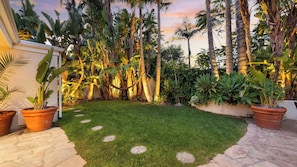 A well-maintained garden with a lawn, stone pathway, and various tropical plants.