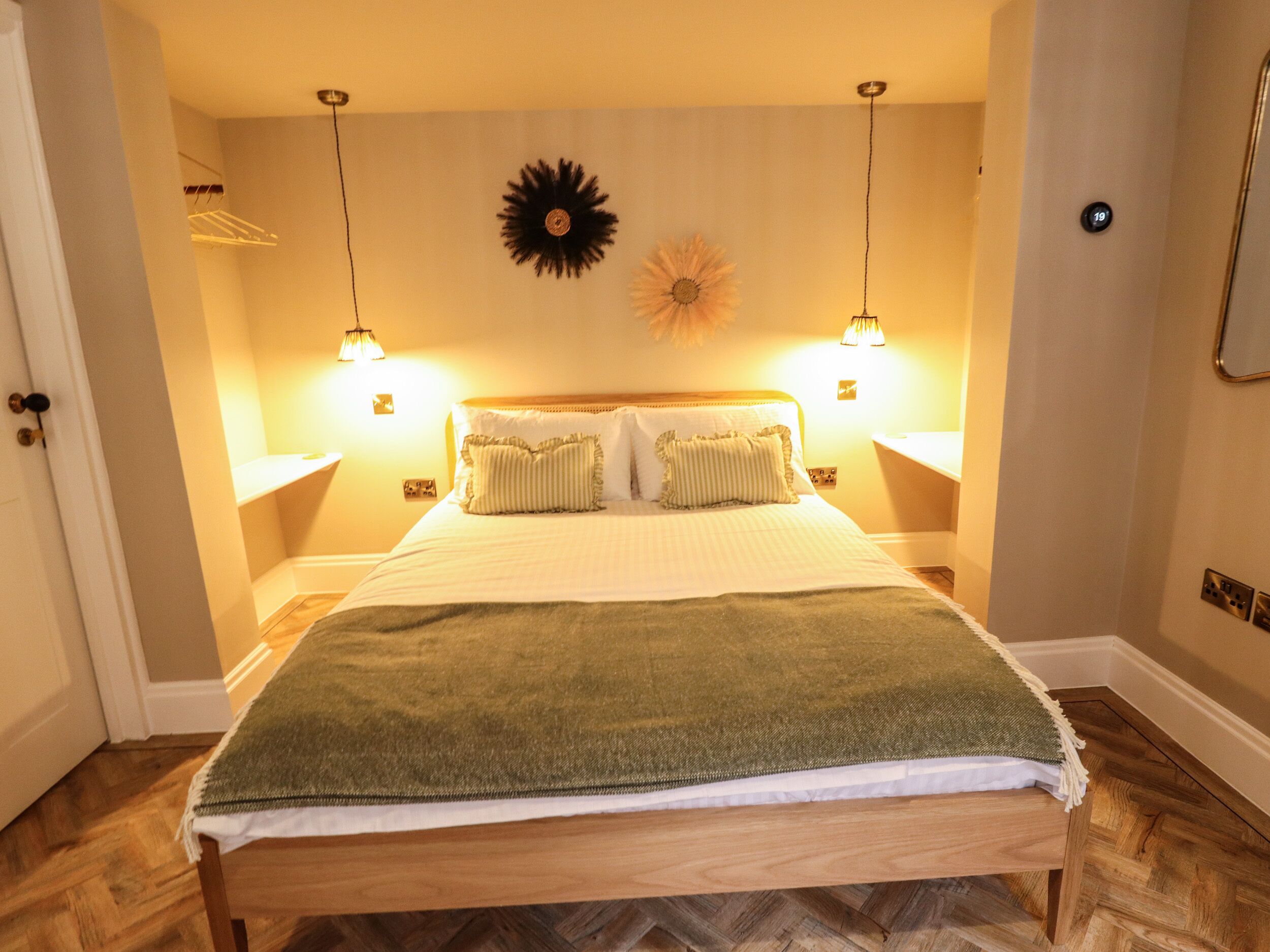 A neatly made bed with a green blanket, two bedside lamps, and a wall clock.