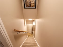 Un pasillo estrecho con una escalera alfombrada, barandal de madera y un cuadro enmarcado en la pared.