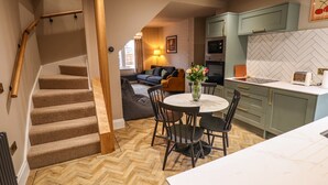 A modern kitchen with a herringbone floor, a dining area with a round table and chairs, and a staircase leading to another level. - 17 Union Road House (Lincoln)