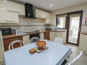 A compact kitchen with a microwave, toaster, and a sink. There is a dining table with chairs and a wooden bowl on it.