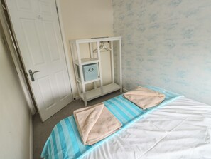 Quarto com cama, duas toalhas, guarda-roupa e porta.