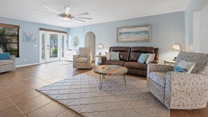 A spacious living room with a brown leather sofa, patterned armchairs, a coffee table, and a ceiling fan.