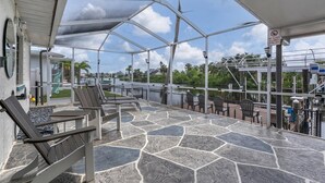 A covered outdoor seating area with stone flooring and metal railings, overlooking a body of water and greenery.