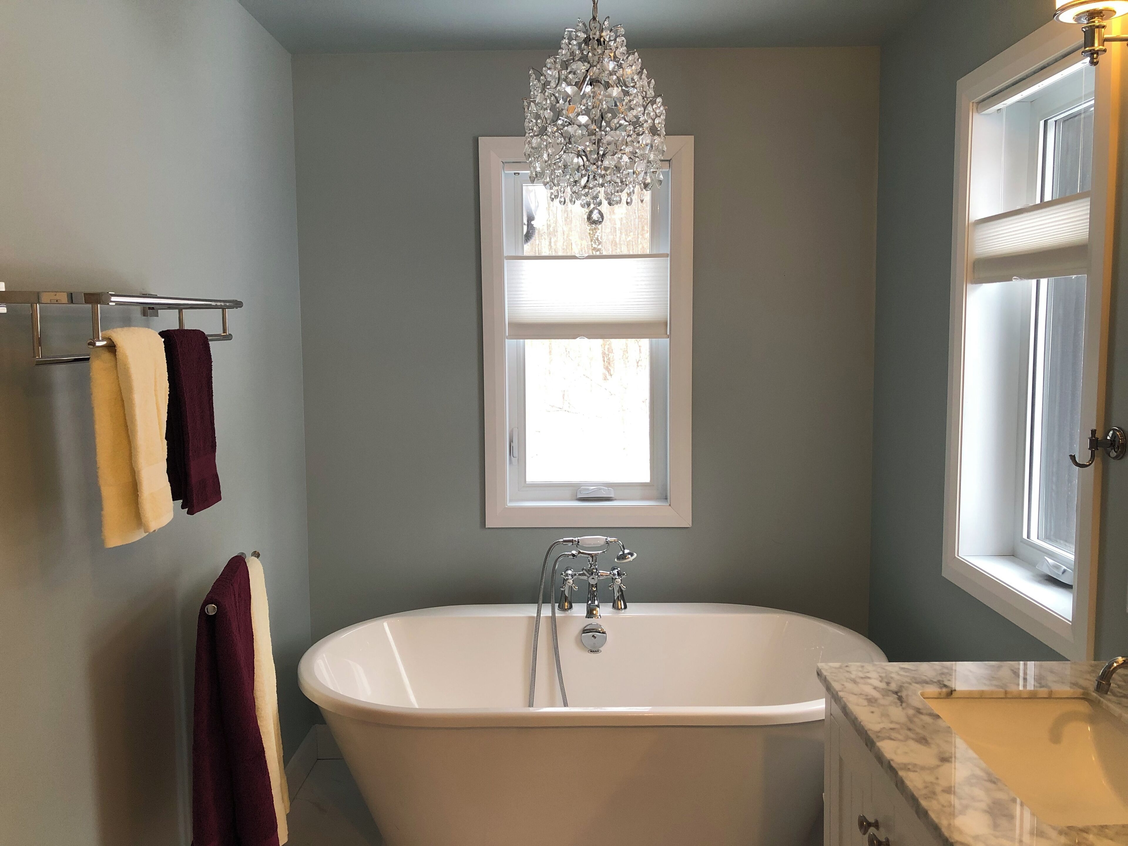 Ein Badezimmer mit freistehender Badewanne, einem Chandelier, einem Fenster mit Jalousien und Handtüchern an einem Halter.
