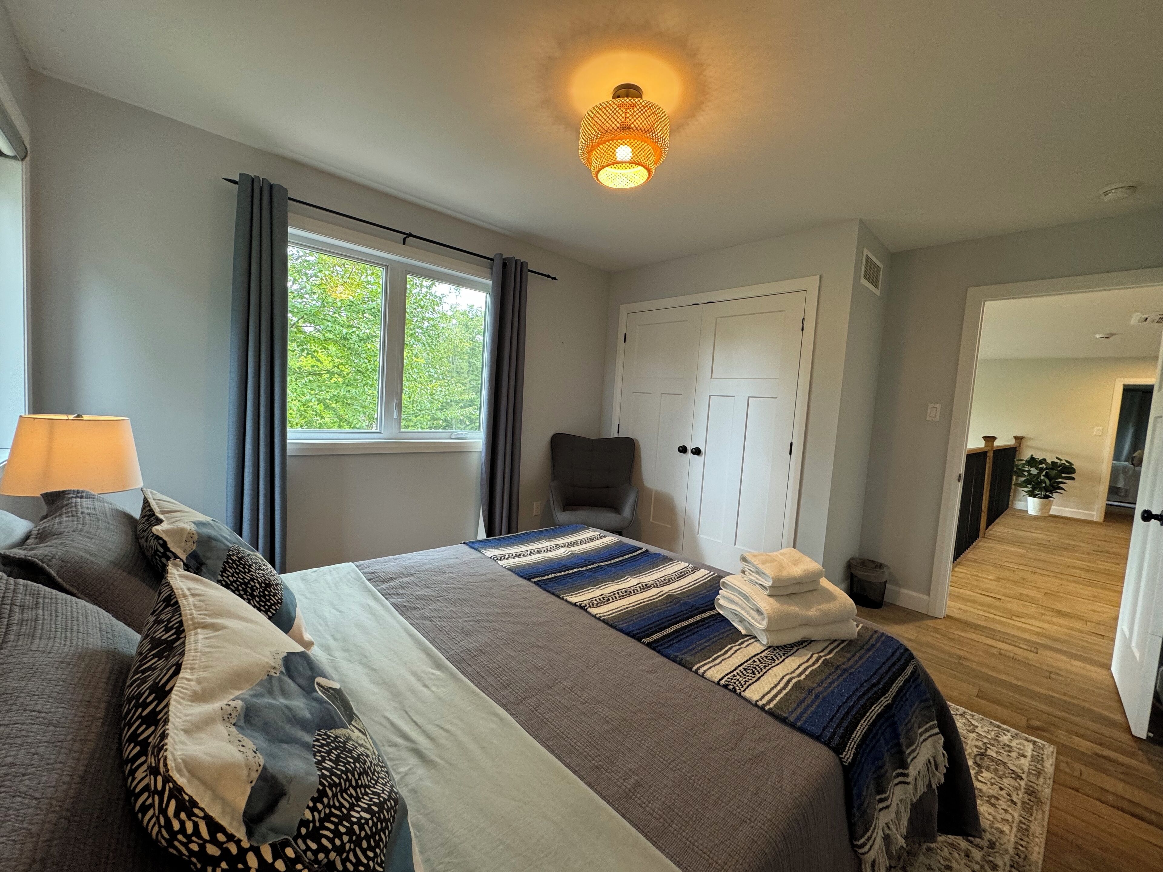 Une chambre d’hôtel avec un lit, une chaise, un bureau, une lampe, une fenêtre et une porte.