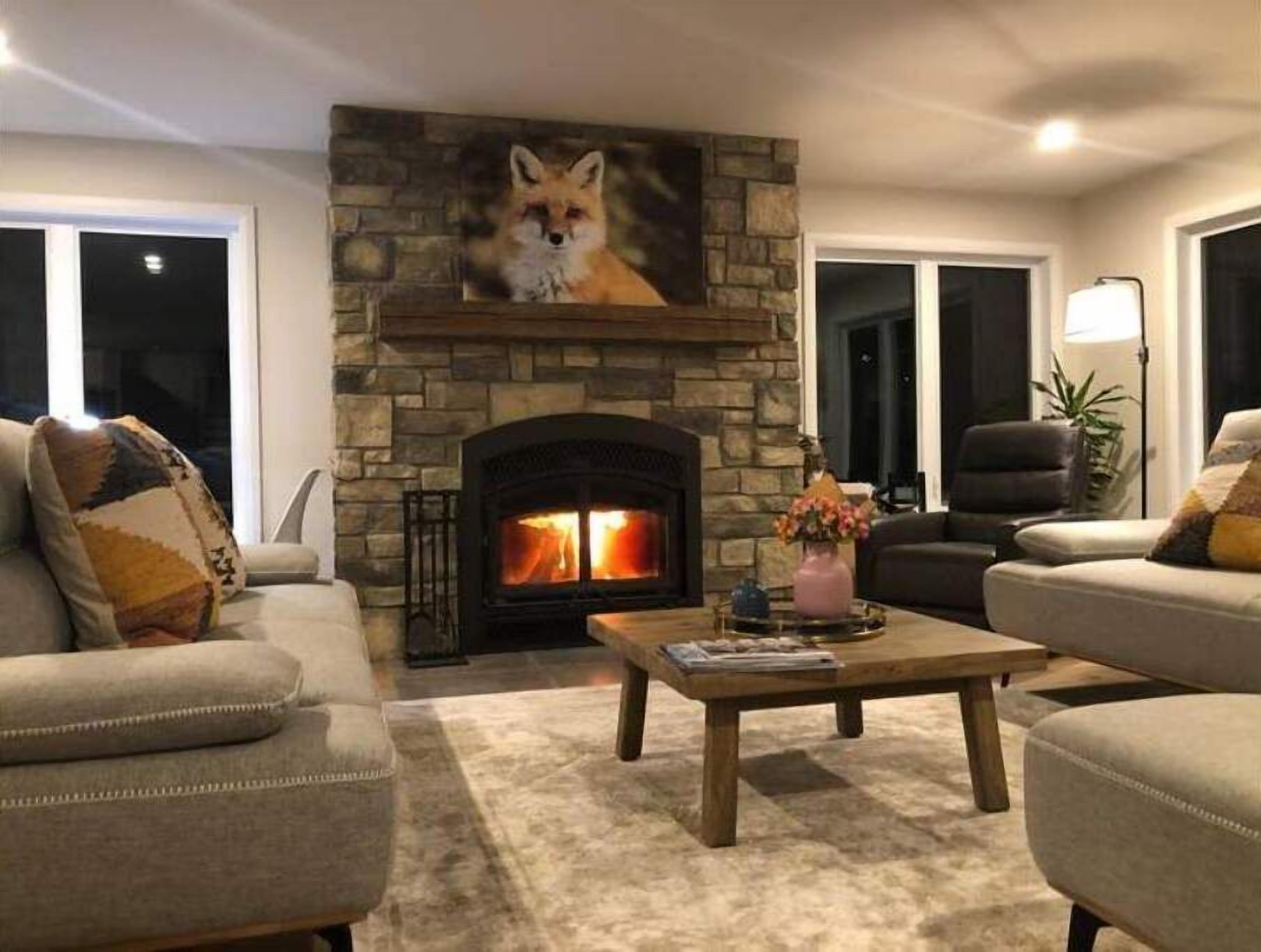 Ein gemütliches Wohnzimmer mit Kamin aus Stein, einer Couch, einem Couchtisch und einem Gemälde von einem Fuchs.