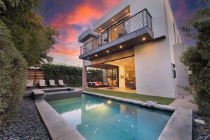 Una casa moderna a due piani con piscina, area salotto esterna e un balcone.