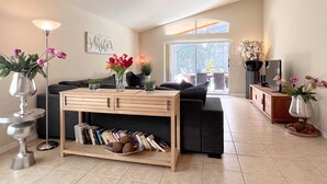 A modern living room with a sofa, coffee table, and bookshelves. There is a TV and a potted plant on a stand.
