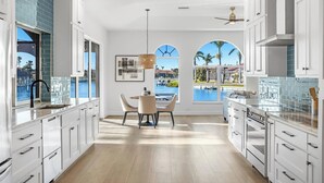 Una cocina moderna con armarios blancos, un comedor con vista a una piscina y un ventilador de techo.