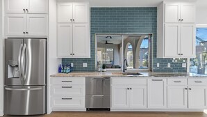 Una cocina moderna con armarios blancos, un refrigerador de acero inoxidable, un lavavajillas y un salpicadero con azulejos verde azulado.